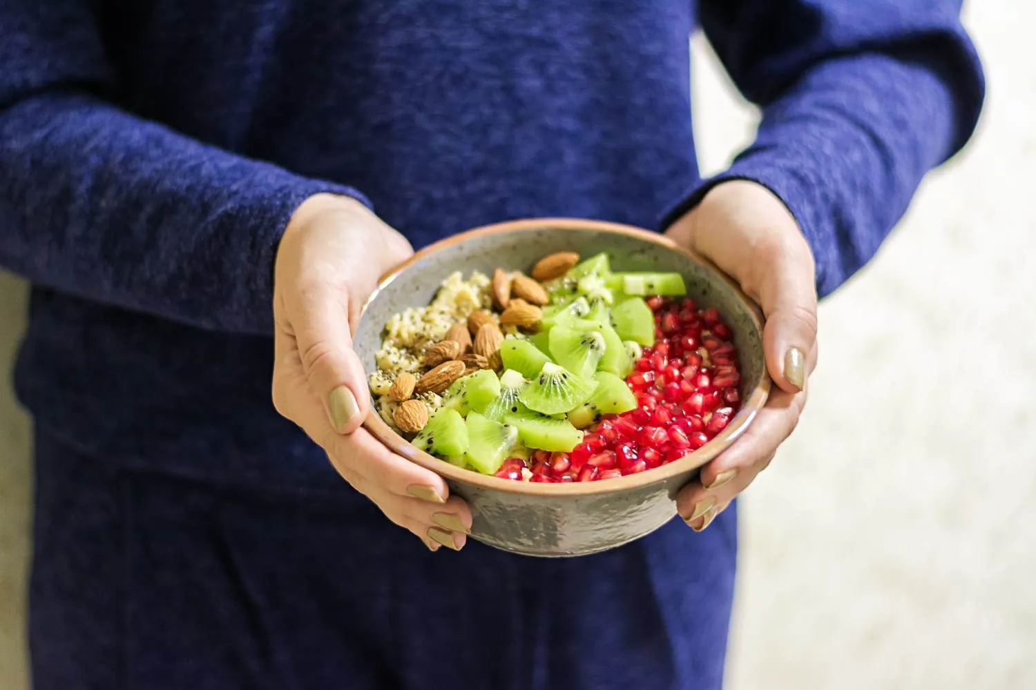 Hands holding a bowl of pomegranate, kiwi and almonds